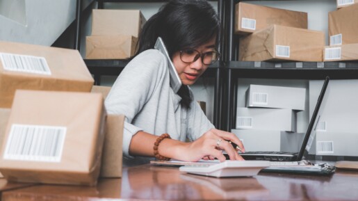 A self-employed woman managing her business from home, calculating expenses while speaking on the phone and using a laptop — representing 1099 professionals exploring private health insurance options.